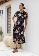 Model poses with one hand in pocket wearing a shirt style button through cotton dress with collar and a removable waist tie.