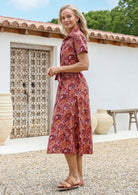 Woman standing in a midi length 1950s style shirt dress with structured collar, short sleeves, waist tie and pockets. 