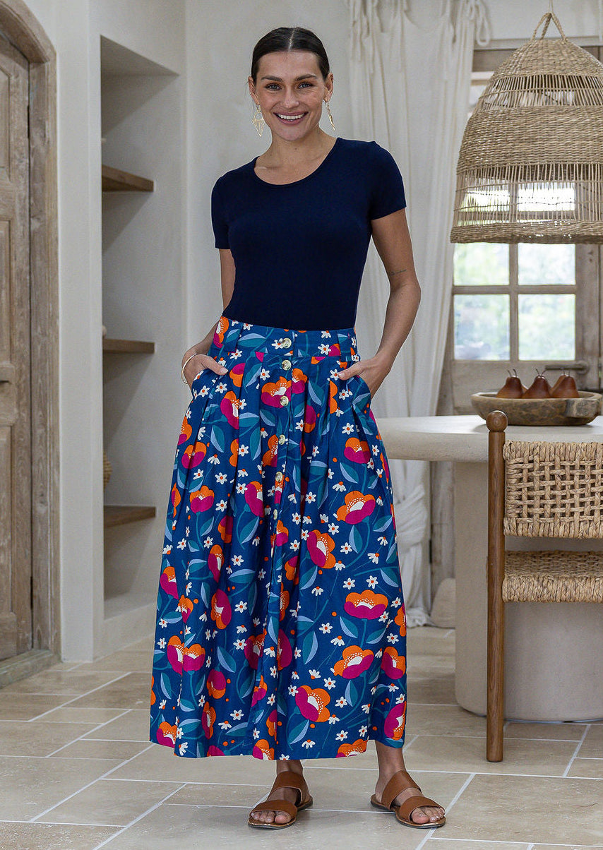 Woman standing with both hand in pockets wears 100% cotton button through skirt in royal blue based floral print. 