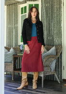 Woman in cotton corduroy red skirt and black jacket standing in a room with wicker furniture.