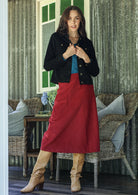 Woman wearing a black cotton corduroy jacket with brass buttons and pockets, [aired with a blue top, red skirt, and tan boots