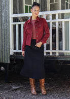 Woman wearing a jacket in deep, luxurious, and intense red-purple hue  standing against a white railing