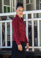 Woman stands sideways wearing a corduroy jacket and black corduroy skirt against a white railing.