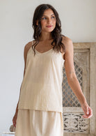 Woman wears lightweight cotton cami in nude tone, with V-neckline, spaghetti straps and a picot trim