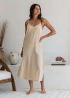 Woman poses wearing nude lightweight cotton maxi slip with V-neckline, bust darts, side splits and picot trim hem