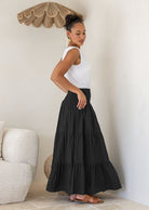 Woman standing side on wearing a white singlet top and black cotton tiered maxi skirt with wide ruched waistband