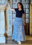 Woman wears a white based blue floral cotton maxi skirt paired with a navy blue stretch t-shirt, leaning on a pillar