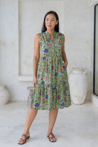 Woman wearing a sleeveless green floral cotton dress with pockets, mandarin collar and a two tiered skirt.
