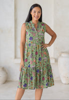 Woman posing in 100% cotton, sleeveless, knee length dress with a V-neckline and buttoned bodice in moss green based multicoloured floral dress.