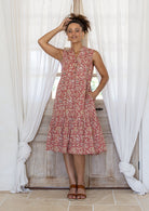 Woman posing in a rose pink based floral sleeveless dress with a buttoned bodice, two tiered skirt and mandarin collar 