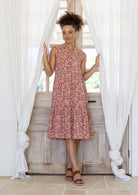 Woman wearing a rose pink based floral sleeveless, knee length dress with a buttoned bodice, tiered skirt and pockets. 