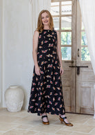 Woman wearing a floral cotton sleeveless maxi dress standing in a room with a wooden door and white curtains.
