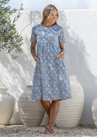 Woman poses in a blue based cotton floral short sleeve dress with round neckline