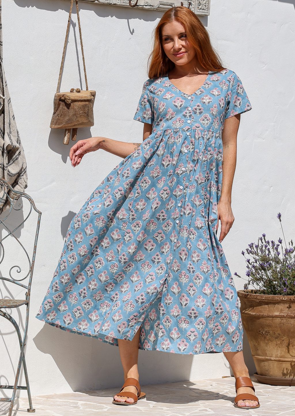 Woman standing in a 100% cotton floral print dress with a V-neckline, short sleeves, pockets, and buttons through to the knee.