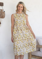 Model wears 100% cotton sleeveless midi dress with high round neckline, tiered design and pockets in cream based floral print