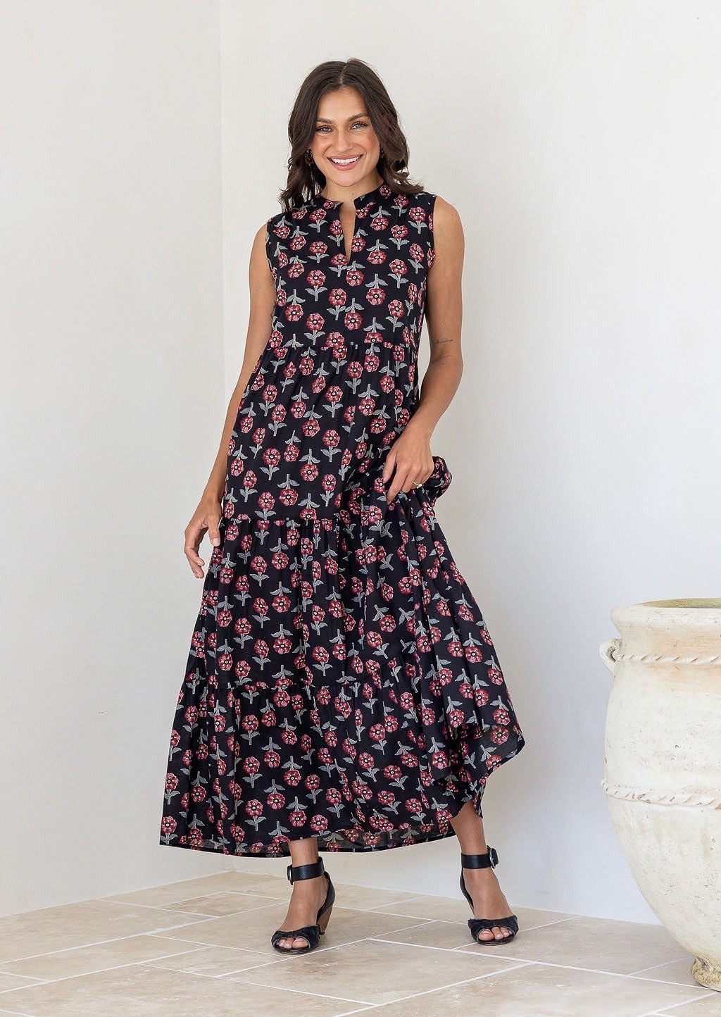 Woman wearing a 100% cotton black floral tiered maxi dress with sleeveless design and notch neckline. 
