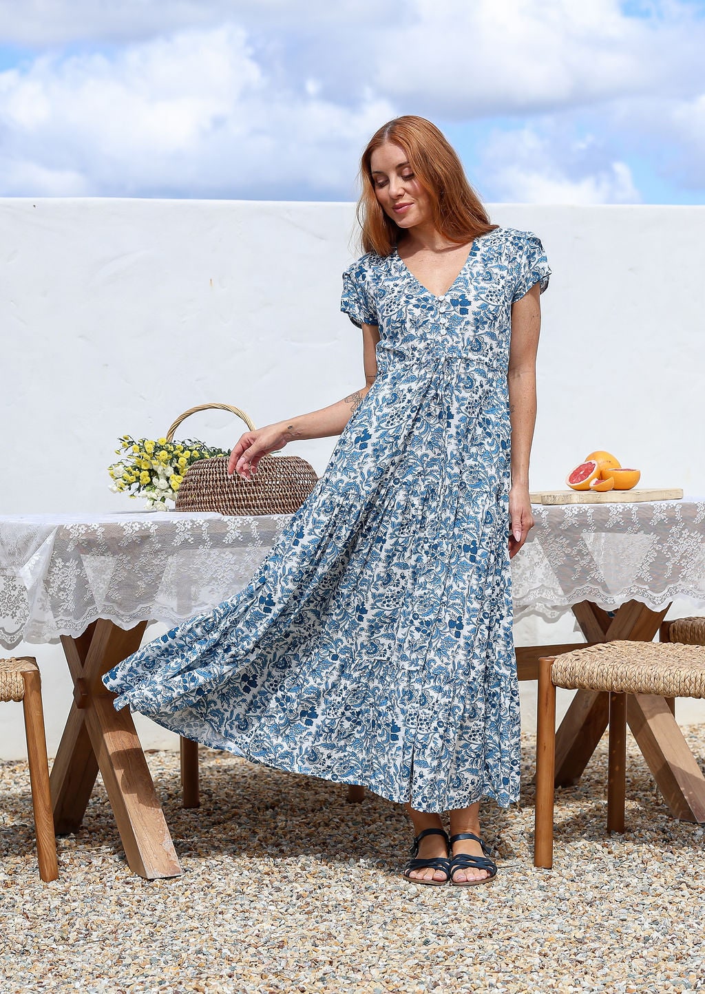 Woman wearing a 100% cotton white based blue floral print maxi dress with V-neck and cap sleeves. 
