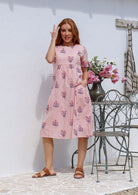 Woman wearing a pink striped white based floral print cotton dress with one hand in pocket.
