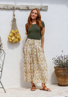 Woman wearing a basic top and floral button through shin length cotton skirt with box pleats, belt loops and pockets.