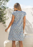 Woman stands backwards wearing a 100% cotton blue based floral dress with round neckline.