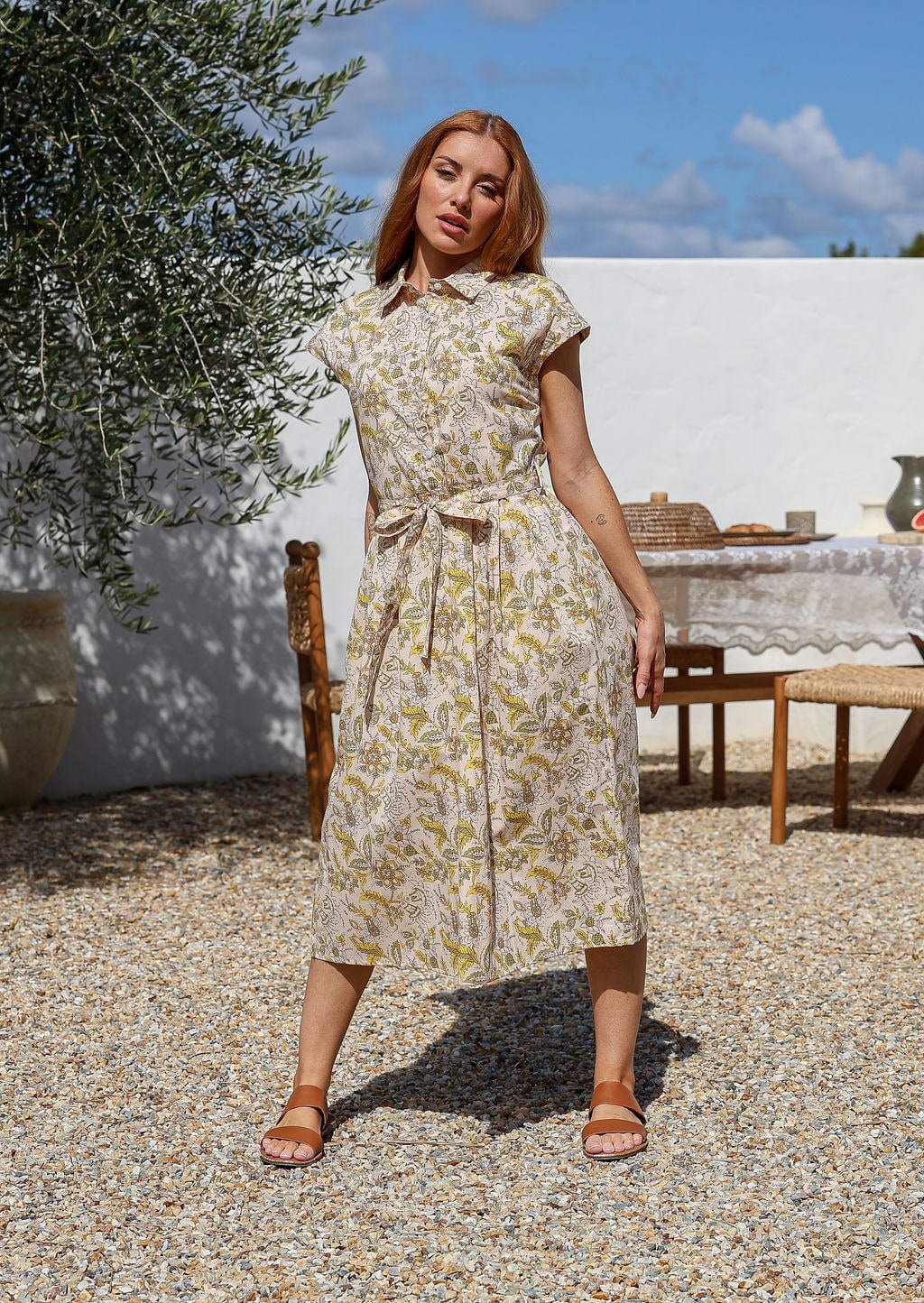 Woman wearing a midi shirt dress with yellow-floral print, belted waist. 