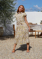 Woman wearing a midi shirt dress with yellow-floral print, belted waist. 