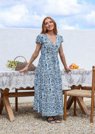 Blue and white floral print maxi dress with V-neck and cap sleeves, worn by model standing outdoors