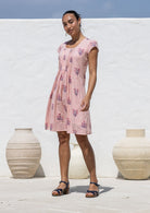 Woman standing wearing a 100% cotton pink striped white based floral dress with round neckline.