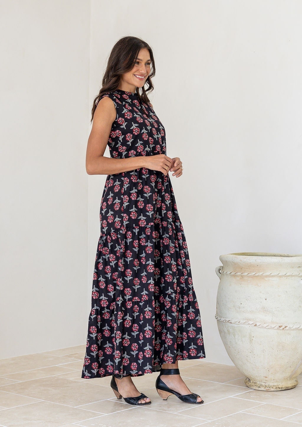 Black floral print tiered maxi dress, sleeveless, on model standing beside large urn.