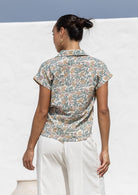 Woman standing backwards wearing a floral cotton top with short folded cuff sleeves, collar and V neckline