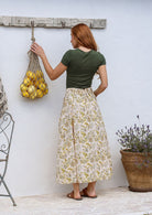 Woman stands backwards wearing a basic top and floral print, shin length cotton skirt with button through front and box pleats.