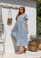 Woman stands sideways wearing a 100% cotton dress with short sleeves, pockets, and a drawstring tie at the back.