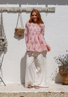 Woman poses in a Pink floral print long-sleeve top with white wide-leg white pants. 