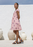 Woman stands sideways wearing a 100% cotton pink striped white based floral short-sleeve dress with round neckline.