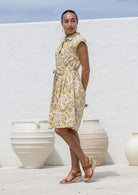 Woman stands sideways wears fit and flare style shirt dress, 100% cotton with collar, cap sleeves, and removable waist tie. 