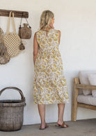 Woman stands backwards wearing a sleeveless cotton midi dress with two tiered design and high round neckline