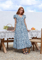 Blue and white floral print maxi dress with V-neck and cap sleeves, worn by model standing outdoors