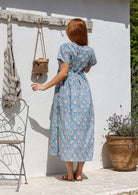 Woman stands backwards wearing a 100% cotton dress with short sleeves, pockets, and a drawstring tie at the back.