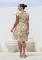 Woman stands backwards wears fit and flare style shirt dress, 100% cotton with collar, cap sleeves, and removable waist tie. 