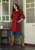 Woman wearing red corduroy A-line tunic dress with 3/4 sleeves with hands in pockets 