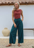 Woman poses in relaxed fit wide-leg cotton pants in deep teal with pockets, elastic waist and drawstring tie.