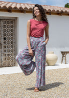 woman wearing wide legged blue based floral print 100% rayon pants and wide neck mod top with hand in pocket
