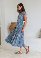 Woman stands sideways wearing a rayon maxi dress with voluminous tiered skirt and buttoned bodice