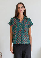 Woman poses in relaxed fit cotton short sleeve top with rolled cuffs sleeves, collar and V neckline.
