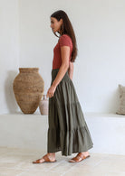 Model standing sideways wearing a three tiered, cotton maxi skirt with scoop neck t-shirt in terracotta.