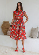 Model posing in a red floral print shirt style 100% cotton dress with cap sleeves and detachable waist tie