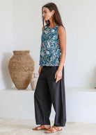 Woman standing sideways wearing a 100% cotton retro floral top, sleeveless design with side bust darts