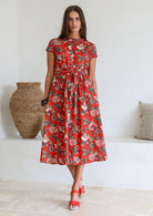 Woman wears retro style cotton button through midi length dress with high round neckline, short sleeves and a removable waist tie.