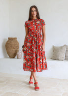Woman poses in 1950's style short sleeved, button through cotton dress with high round neckline in red based floral print.