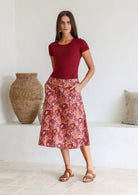 Woman wearing a basic maroon top and warm toned floral a-line cotton skirt with side zipper and both hands in pocket.